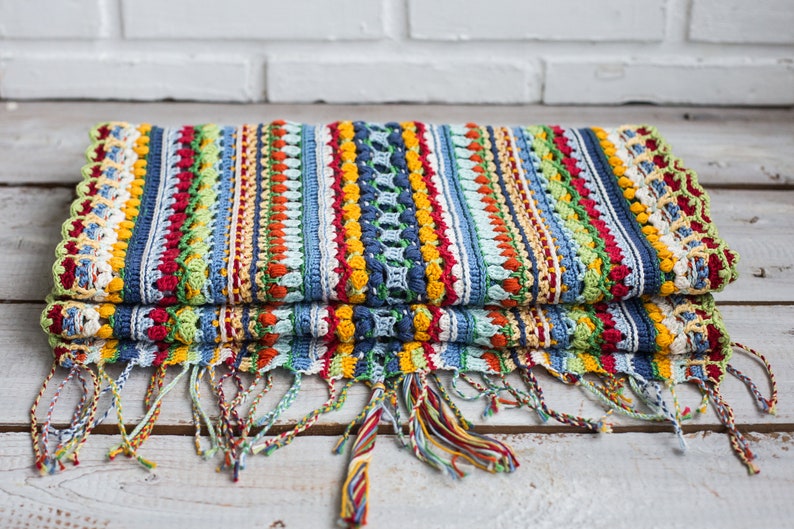 A scarf made by hand using crochet techniques, featuring tassels in vibrant primary colors.