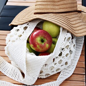 May include: A white crocheted bag filled with green and red apples, with a straw sun hat on top of the bag.