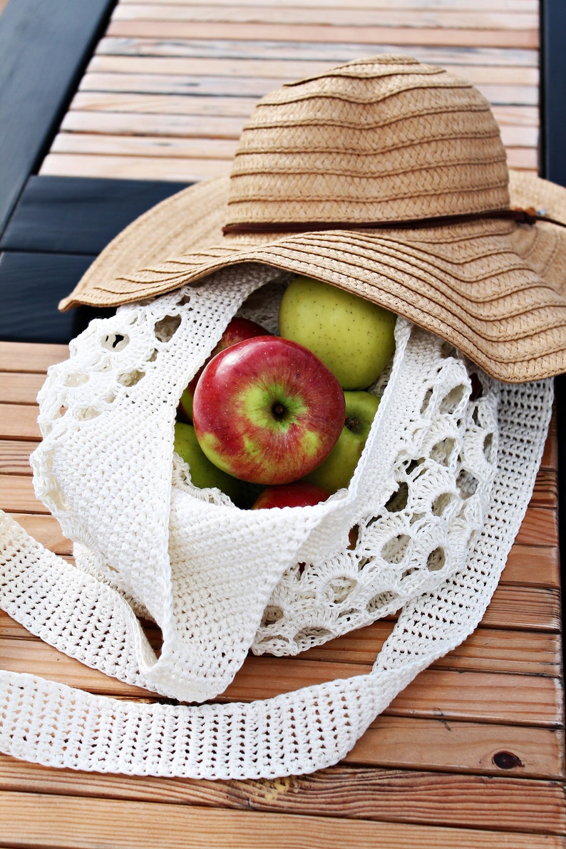May include: A white crocheted bag filled with green and red apples, with a straw sun hat on top of the bag.