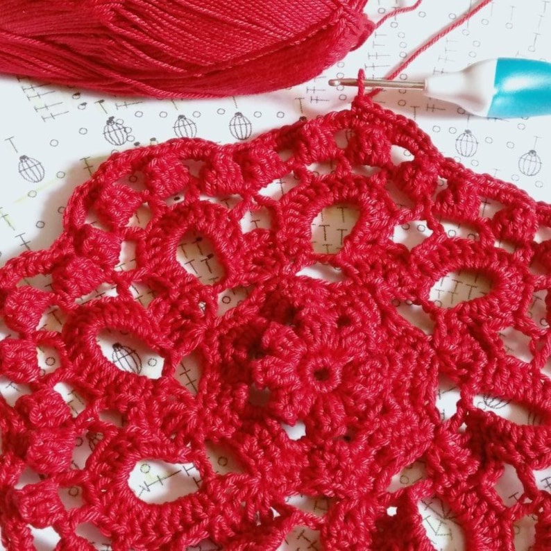 May include: A close-up of a red crocheted doily with a detailed floral pattern. The doily is being worked on with a crochet hook and red yarn.