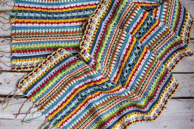 A beautiful multi-colored scarf with fringe is displayed on a light wooden background.