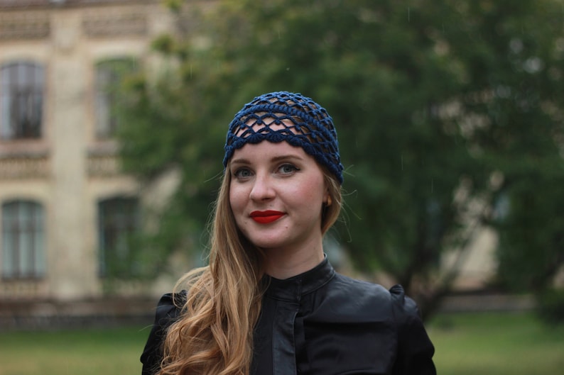 May include: A woman with long blonde hair wearing a blue crocheted hat and a black mock neck shirt.