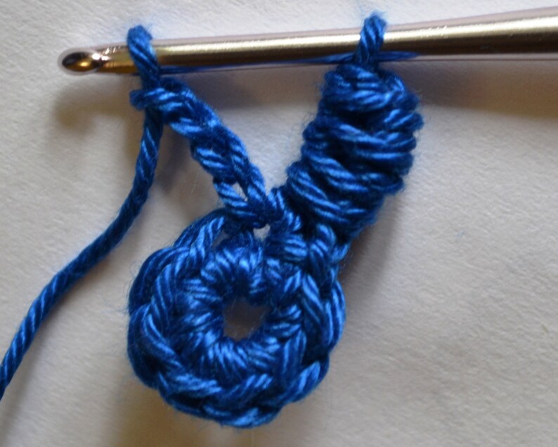 May include: A close-up of a blue crochet flower with a crochet hook and yarn attached.