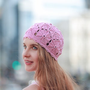 A woman in a crocheted cotton pink beret with a textured pattern of pentagons is smiling.