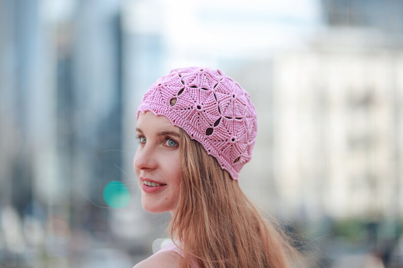 A woman in a crocheted cotton pink beret with a textured pattern of pentagons is smiling.