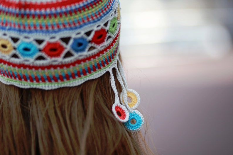 May include: A colorful crocheted hat with a white crocheted tassel and colorful crocheted circles hanging from the tassel.