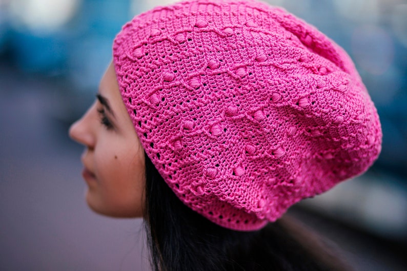 A crochet pink hat is showcased on the side profile of a woman's head.
