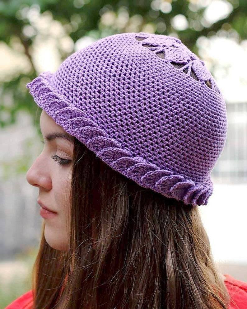 A purple crocheted hat with a lacy design (moss stitch and lacy leaves) on the top and a scalloped brim.