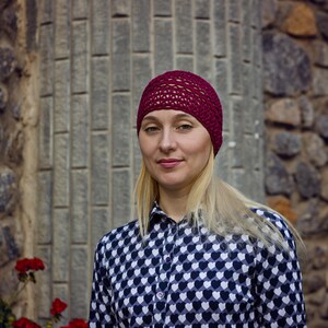 May include: A woman with blonde hair is wearing a burgundy knit hat and a black and white shirt with a heart pattern.