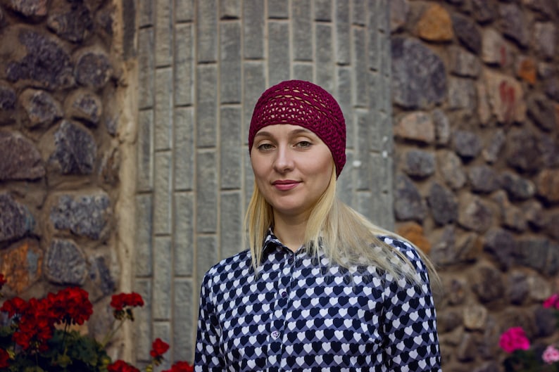 May include: A woman with blonde hair is wearing a burgundy knit hat and a black and white shirt with a heart pattern.