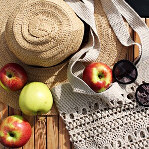 May include: A straw hat, a crocheted tote bag, apples, and sunglasses on a wooden surface.