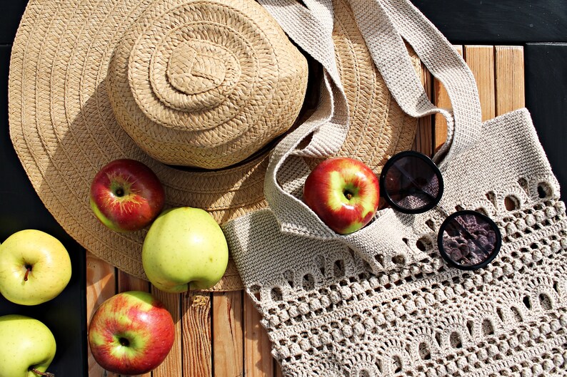 May include: A straw hat, a crocheted tote bag, apples, and sunglasses on a wooden surface.
