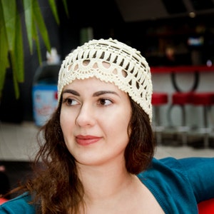 May include: A woman with long brown hair wearing a white crocheted hat and a teal blue cardigan.