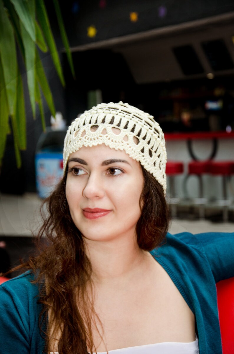 May include: A woman with long brown hair wearing a white crocheted hat and a teal blue cardigan.
