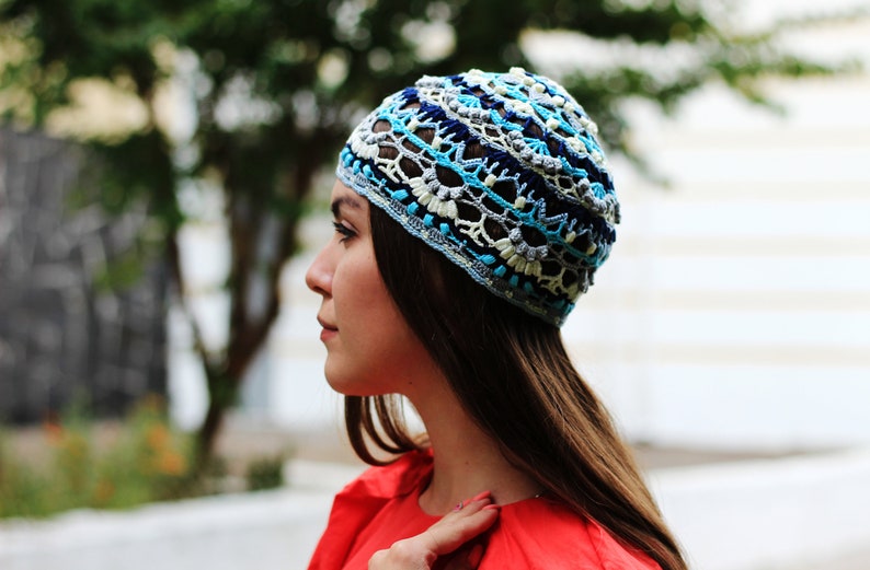 May include: A woman wearing a blue, white, and gray crocheted hat. The hat has a geometric pattern and is worn on her head.