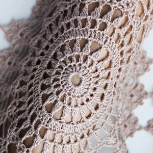 Close-up of large round crochet motif in beige linen yarn, showing delicate lace pattern and intricate stitch work.