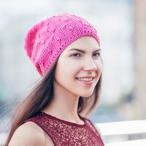 A woman stands partially turned, displaying an exquisite handmade crochet slouchy hat with a textured pattern.