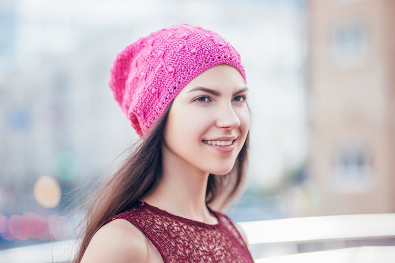 A woman stands partially turned, displaying an exquisite handmade crochet slouchy hat with a textured pattern.