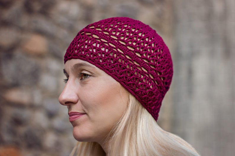 May include: A close-up of a woman wearing a burgundy crocheted beanie hat. The hat has a delicate openwork design.