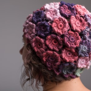 Könnte beinhalten: Eine gehäkelte Mütze mit einem Blumenmuster in den Farben Rosa, Lila und Grau.
