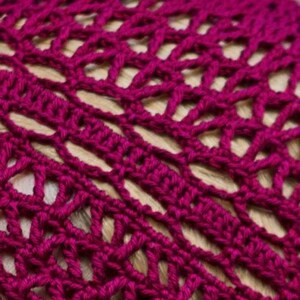 May include: Close-up of a crocheted hat in a deep magenta color. The hat has a delicate openwork pattern.