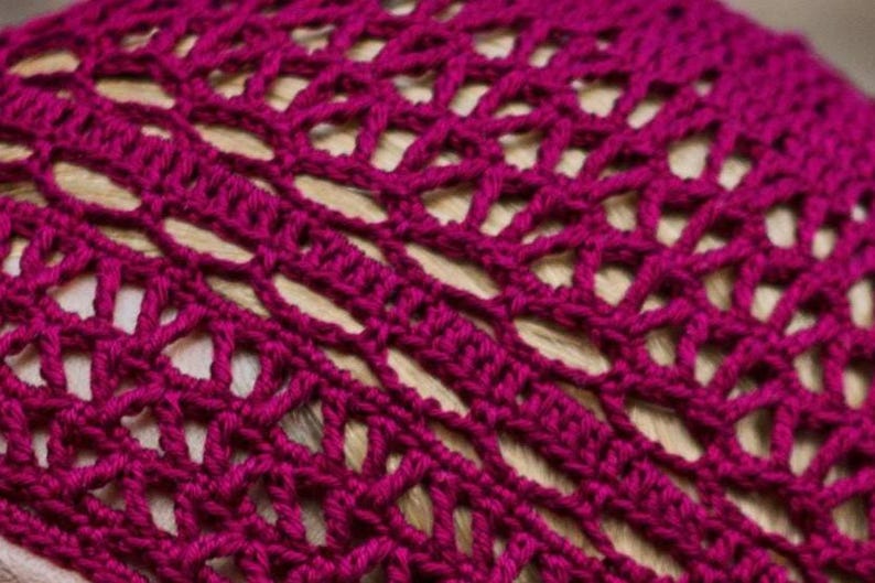 May include: Close-up of a crocheted hat in a deep magenta color. The hat has a delicate openwork pattern.