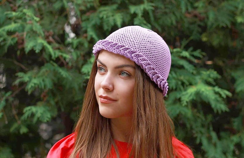 A purple crocheted hat with a scalloped edge. The hat is worn by a person with long brown hair. Breathable mesh design for summer.