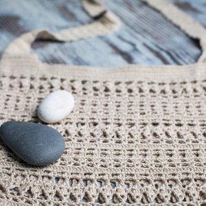 May include: A beige crocheted tote bag with a white and a gray stone resting on top.