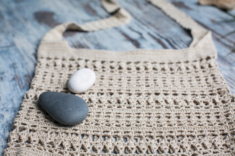 May include: A beige crocheted tote bag with a white and a gray stone resting on top.