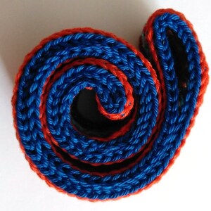 K&ouml;nnte beinhalten: Nahaufnahme eines aufgerollten geflochtenen Seils in Blau und Orange. Das Seil ist mit einem dicken, strukturierten Muster gewebt.