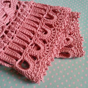 May include: A close-up of a pink crocheted lace fabric with a delicate pattern. The fabric has a soft, airy texture and is perfect for adding a touch of elegance to any project.