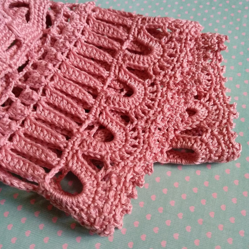 May include: A close-up of a pink crocheted lace fabric with a delicate pattern. The fabric has a soft, airy texture and is perfect for adding a touch of elegance to any project.