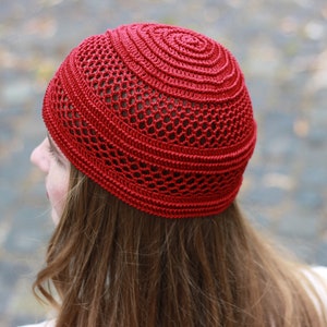 May include: A red crocheted beanie with a lacy pattern. The beanie is worn on a person's head.