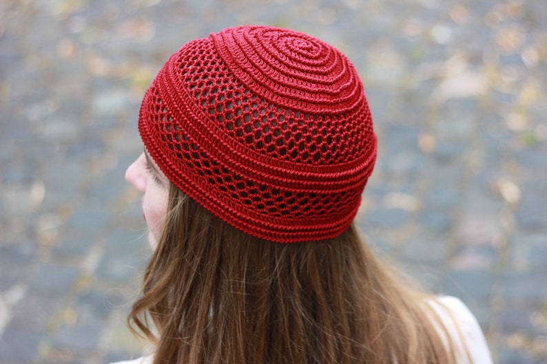 May include: A red crocheted beanie with a lacy pattern. The beanie is worn on a person's head.