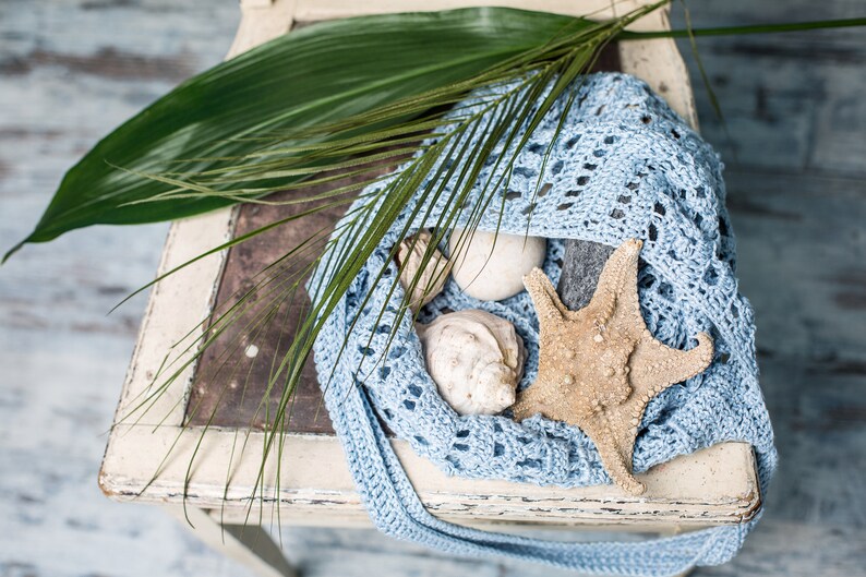 Delicate half-moon shaped crochet bag, shown in soft blue with beach-inspired styling – perfect for sunny days