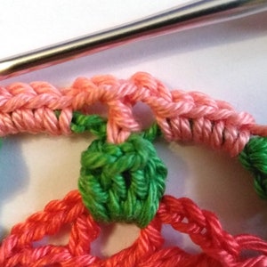 May include: Close-up of a crocheted doily with pink, green, and red yarn. The doily is being worked on with a crochet hook.