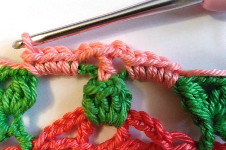 May include: Close-up of a crocheted doily with pink, green, and red yarn. The doily is being worked on with a crochet hook.