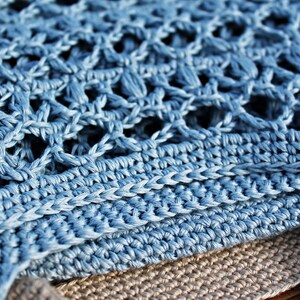May include: A close-up of a blue crocheted fabric with a textured pattern. The fabric is folded over itself, revealing a layer of beige fabric underneath.