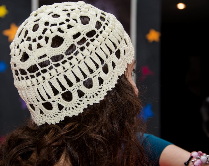 May include: A white crocheted hat with a delicate lace pattern. The hat is worn by a person with long brown hair.