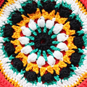 May include: Close-up of a colorful crocheted round mat with a central design of black, white, green, and yellow yarn. The mat has a red border with a green and white trim.