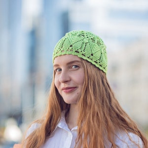 May include: A woman with long, red hair is wearing a light green crocheted hat. She is smiling and looking to the side.