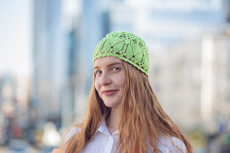 May include: A woman with long, red hair is wearing a light green crocheted hat. She is smiling and looking to the side.