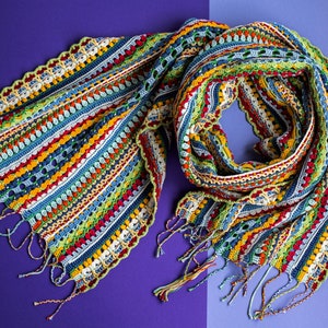 The twisted multicolor crohet scarf lies on a purple background.