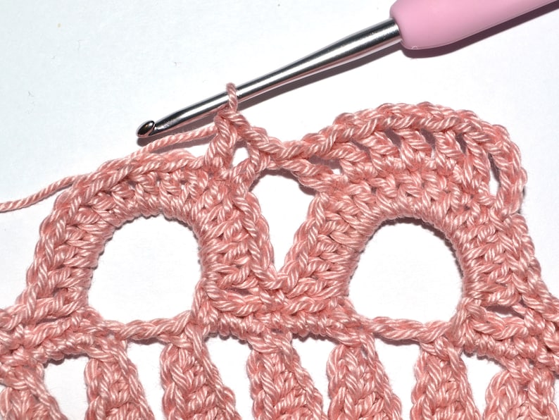 May include: Close-up of a pink crochet project with a crochet hook in the loop of the last stitch. The crochet project has a repeating pattern of circles.