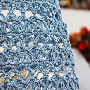May include: Close-up of a light blue crocheted fabric with a delicate pattern. The fabric has a soft, textured appearance.