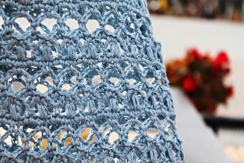 May include: Close-up of a light blue crocheted fabric with a delicate pattern. The fabric has a soft, textured appearance.
