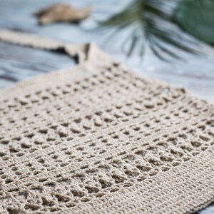 May include: A close-up of a beige crocheted tote bag with a simple, open-weave design. The bag is made of natural fibers and has a relaxed, bohemian style.
