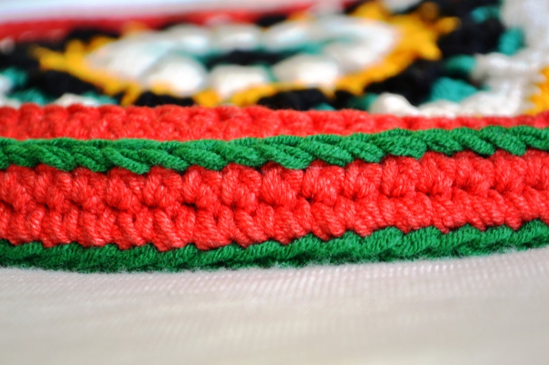 May include: Close-up of a red and green crocheted border. The border is made of yarn and has a textured, woven look.