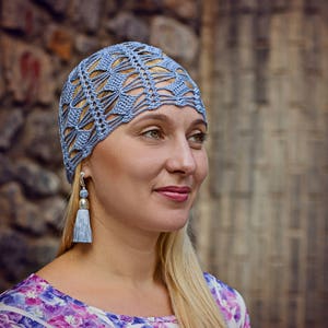 A lace crochet blue hat is worn by a woman facing the camera.