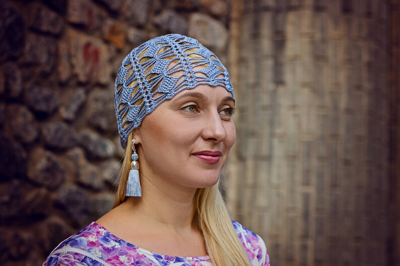 A lace crochet blue hat is worn by a woman facing the camera.